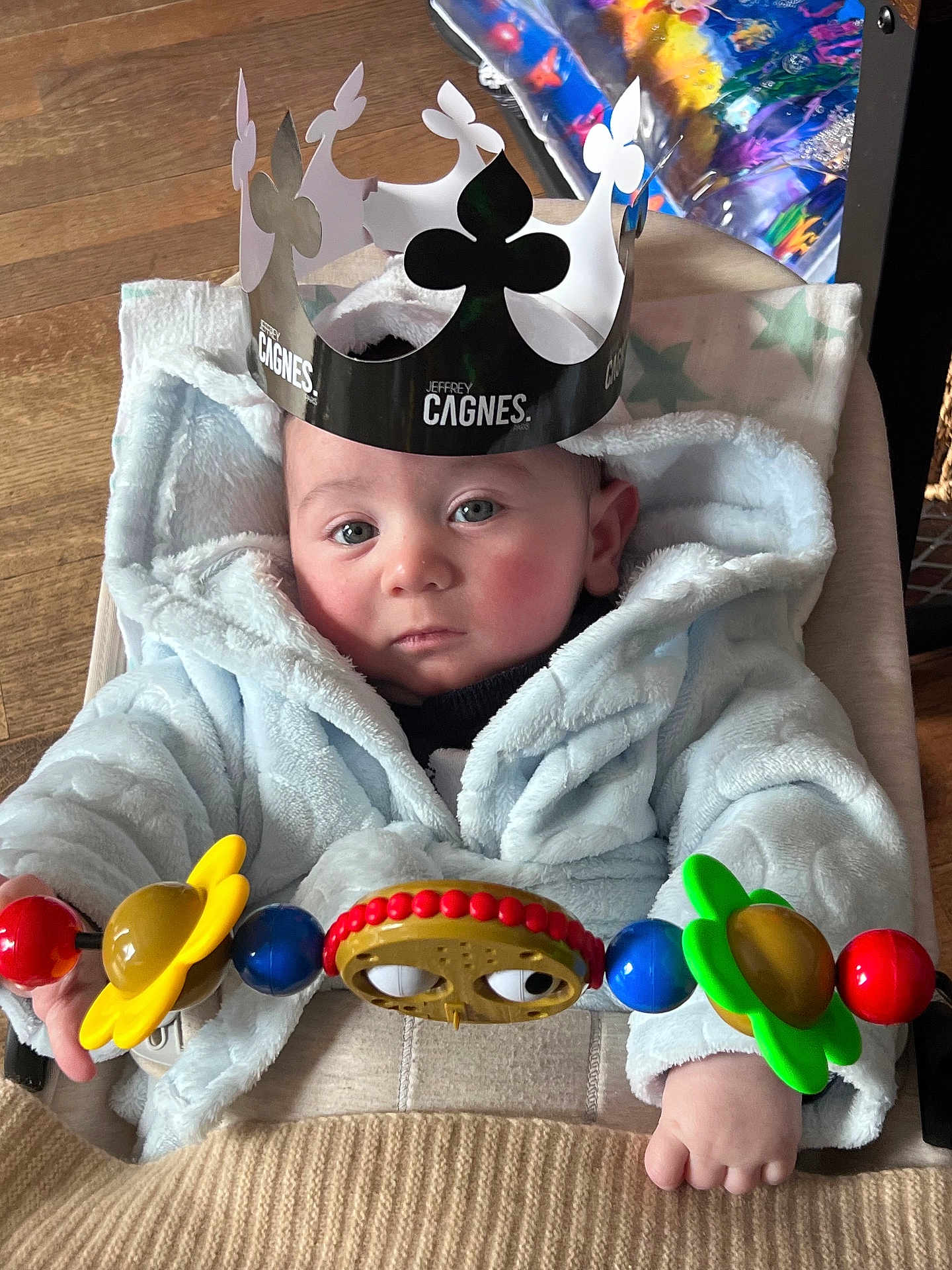 Harper a rejoint le concours — aidez-le/la à gagner de superbes lots ! baby, child, hoodie, crown, toy, flower, stroller, hand, face, blue, red, yellow, green, indoor, wood_floor, blanket, person, portrait, cute, expression