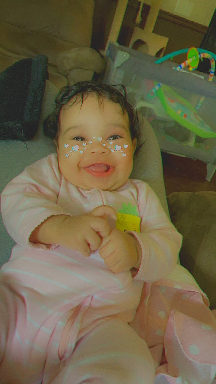 Lucille is registered to the contest to win money with this photo: baby, baby_products, baby_toddler_clothing, cheek, comfort, eye, fun, gesture, happy, human_body, iris, joy, linens, lip, mouth, nose, person, sitting, skin, smile