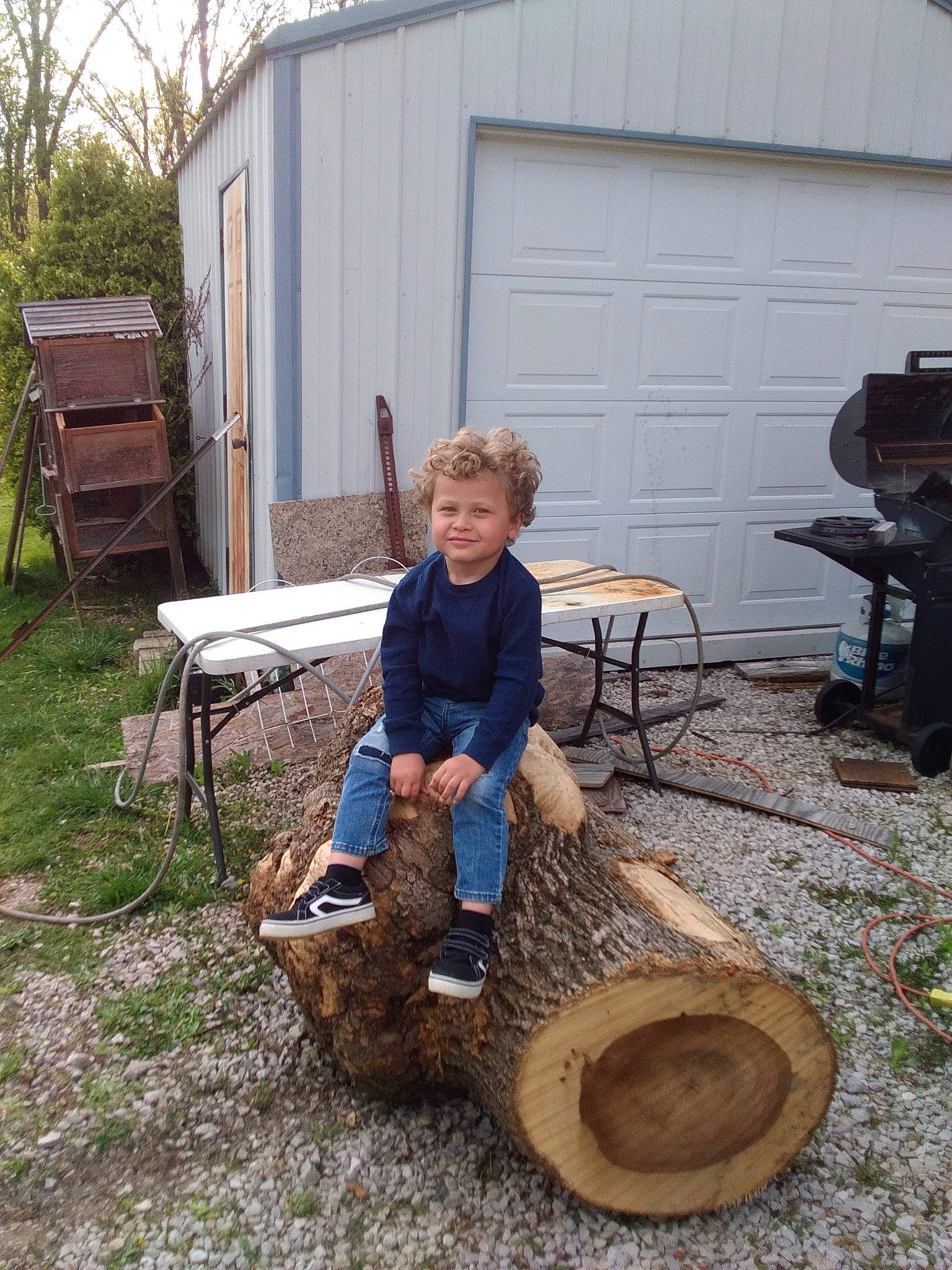 Jordan is registered to the contest to win money with this photo: automotive_tire, automotive_wheel_system, chair, door, grass, hat, joy, landscape, leisure, outdoor_furniture, outdoor_table, person, plant, shorts, sitting, soil, table, tire, tree, trunk