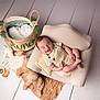 baby, infant, sleeping, chair, cushion, stuffed_toy, basket, blanket, floor, wooden_floor, plush, cute, peaceful, indoors, soft_toys, child, portrait, smiling, relaxed, comfortable