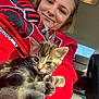 Stormy Mae is registered to the contest to win money with this photo: person, kitten, cat, animal, feline, indoor, car_interior, red_hoodie, smile, young_adult, closeup, pet, cute, cozy, seated, window, seat, seatbelt, daylight, casual