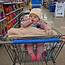 adult, aisle, baby, beanie, blanket, floor, infant, lighting, mall, person, portrait, retail, shelves, shopping, shopping_cart, signage, socks, store, sweater, toy