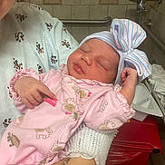 Bianca is registered to the contest to win money with this photo: newborn, baby, infant, hospital, person, pink_onesie, hat, bow, sleeping, arm, hand, patterned_gown, face, cute, child, medical, indoor, tiled_wall, cradle, resting