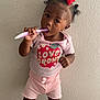 brushing_teeth, carpet, child, curly_hair, cute, girl, home, indoor, person, pink_shirt, portrait, red_bow, red_sandals, serious, shorts, standing, toddler, toothbrush, wall, young_child