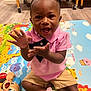 toddler, child, pink_bow, pink_shirt, clapping, play_mat, toy, smiling, happy, indoor, nursery, floor, shorts, black_shoes, baby, person, cute, young_child, playful, colorful