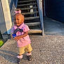 Kehlani is registered to the contest to win money with this photo: black_shoes, building, casual_clothing, child, concrete, curly_hair, door, holding_object, outdoor, person, pink_bow, pink_shirt, pink_socks, shadow, shorts, sidewalk, stairs, sunlight, toddler, young_child