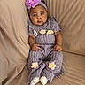 baby, beige_background, casual, child, comfortable, couch, cozy_clothing, curious_expression, cute, flower_decor, flower_headband, headband, indoor, infant, portrait, purple_outfit, sitting, small_hands, soft_fabric, white_socks
