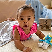 Dream is registered to the contest to win money with this photo: baby, infant, child, pink_clothing, plush_toy, smurf, wooden_block, age_marker, floor, carpet, blanket, indoor, natural_light, curious, wide_eyes, cute, portrait, laying_down, soft_texture, home