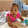 baby, infant, child, pink_clothing, plush_toy, smurf, wooden_block, age_marker, floor, carpet, blanket, indoor, natural_light, curious, wide_eyes, cute, portrait, laying_down, soft_texture, home