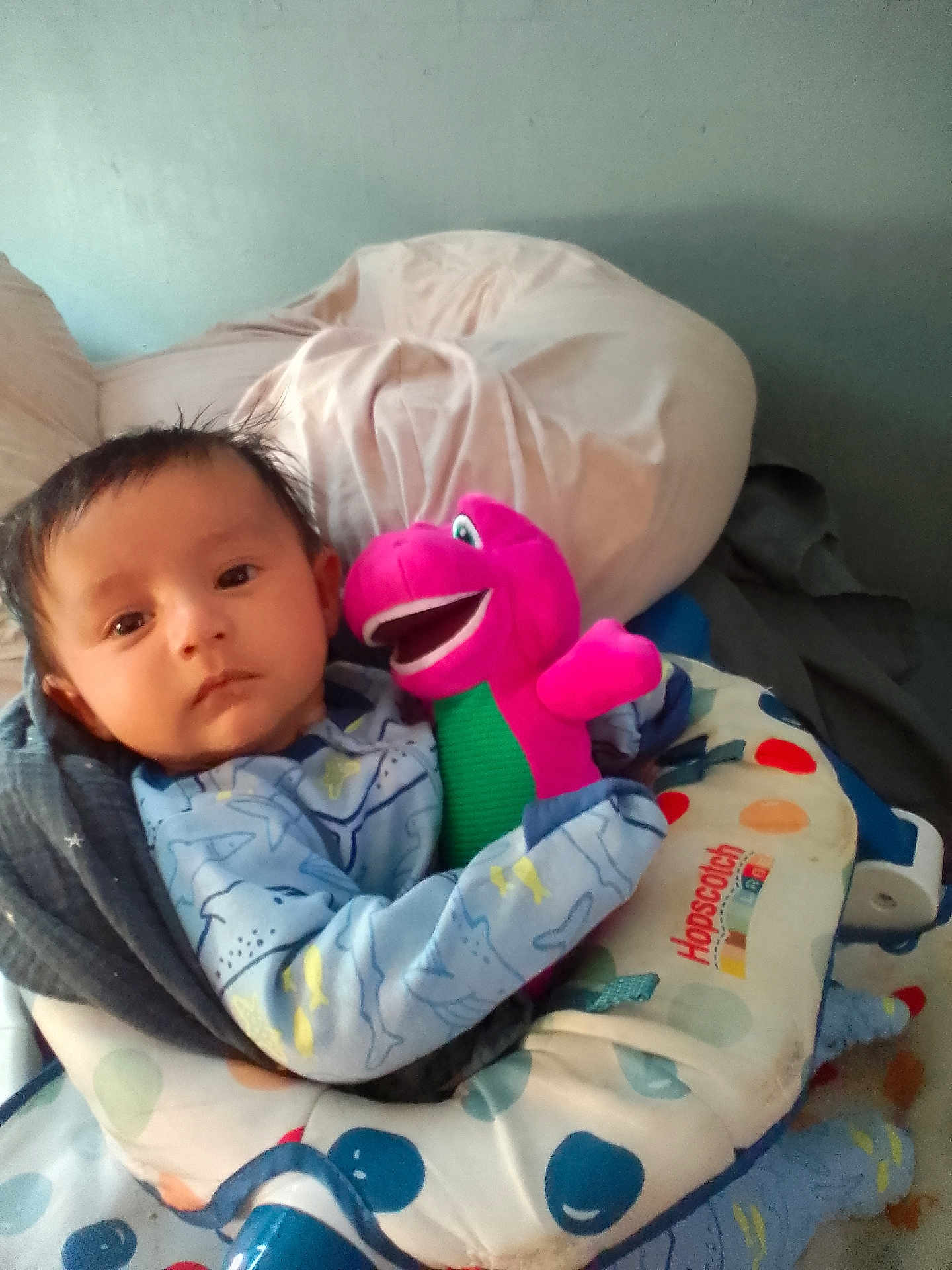 Victor is registered to the contest to win money with this photo: baby, infant, plush_toy, dinosaur, blanket, baby_seat, hopscotch, pillow, blue_clothing, indoors, child, face, cute, resting, soft_toy, colorful, comfort, young_child, portrait, cozy