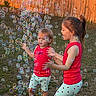 Riverlynn is registered to the contest to win money with this photo: child, children, bubble, bubbles, playing, outdoor, grass, fence, red_clothing, shorts, happy, smiling, toddler, girl, sunlight, daylight, fun, yard, person, nature