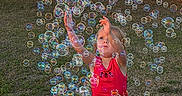 Lakelynn joined the competition — help win amazing prizes! child, toddler, bubbles, outdoor, grass, fence, sunlight, playing, reaching, red_tank_top, shorts, ladybug_print, happy, summer, fun, joy, nature, colorful, daylight, activity
