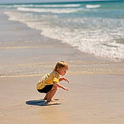 Lakelynn is registered to the contest to win money with this photo: child, beach, sand, ocean, water, waves, yellow_shirt, shorts, barefoot, sunny, nature, outdoor, curious, squatting, shore, reflection, sky, sea, summer, vacation