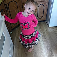 Violet is registered to the contest to win money with this photo: child, girl, smiling, pink_clothing, butterfly_design, skirt, barefoot, kitchen, wooden_floor, cabinet, appliance, curly_hair, playful, pose, indoors, young, person, flooring, standing, bright