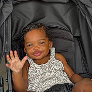 Ariyah is registered to the contest to win money with this photo: toddler, child, stroller, smiling, waving, leopard_print, clothing, seatbelt, black, cute, happy, baby, portrait, person, sitting, young_child, outdoor, skin, face, hand