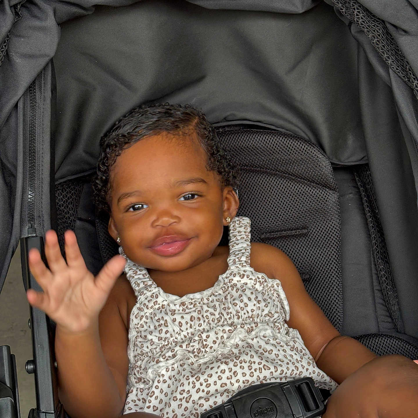 Ariyah is registered to the contest to win money with this photo: toddler, child, stroller, smiling, waving, leopard_print, clothing, seatbelt, black, cute, happy, baby, portrait, person, sitting, young_child, outdoor, skin, face, hand