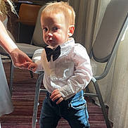 Ashton Tate joined the competition — help win amazing prizes! child, indoor, boy, standing, bow_tie, white_shirt, jeans, brown_shoes, carpet, hand_holding, curtains, chair, light, shadow, portrait, cute, casual_clothing, toddler, small_child, person