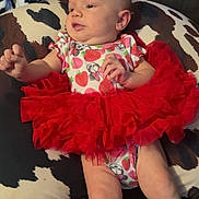 Oakley is registered to the contest to win money with this photo: baby, infant, tutu, red_skirt, onesie, strawberry_pattern, minnie_mouse, pillow, cow_print, couch, furniture, child, person, skin, legs, arms, head, face, indoor, relaxing