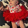 baby, infant, tutu, red_skirt, onesie, strawberry_pattern, minnie_mouse, pillow, cow_print, couch, furniture, child, person, skin, legs, arms, head, face, indoor, relaxing