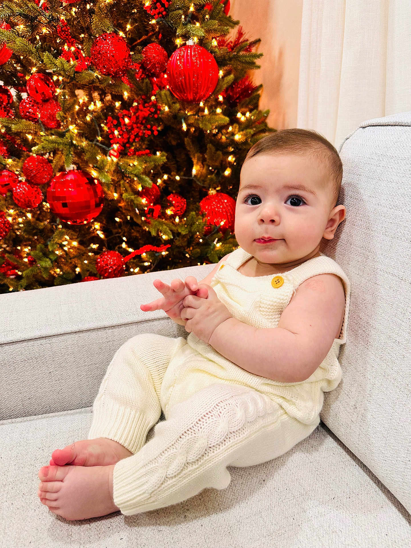 Ashur is registered to the contest to win money with this photo: baby, infant, child, knitwear, cream, couch, christmas_tree, red_baubles, lights, holiday, festive, indoors, portrait, sitting, cute, hands, feet, face, warm_lighting, decorations