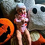 baby, carpet, child, cozy, cute, decor, festive, ghost_pillow, halloween, hat, holiday, indoors, infant, jack_o_lantern, onesie, pacifier, plush_pillow, pumpkin, smiling, soft_toy