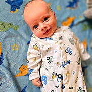 Tommy is registered to the contest to win money with this photo: animal_pattern, baby, blanket, blue, child, comfort, cozy, cute, face, happy, indoors, infant, lying_down, onesie, patterned, portrait, smiling, soft, tractor_pattern, young