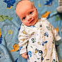 animal_pattern, baby, blanket, blue, child, comfort, cozy, cute, face, happy, indoors, infant, lying_down, onesie, patterned, portrait, smiling, soft, tractor_pattern, young