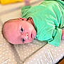 baby, infant, child, green_shirt, blue_eyes, face, skin, polka_dots, changing_pad, soft_surface, curious, lying_down, indoors, closeup, portrait, newborn, expression, cute, human, toddler