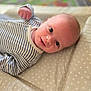baby, infant, smile, face, eyes, clothing, striped, onesie, padded_surface, polka_dot, lying_down, closeup, cute, portrait, child, young, soft_focus, indoor, baby_boy, happy