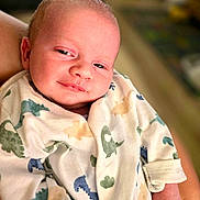 Tommy is registered to the contest to win money with this photo: baby, infant, onesie, dinosaur_pattern, smile, face, hand, person, clothing, cute, newborn, portrait, expression, skin, baby_clothes, sleepwear, child, holding, cozy, soft_lighting