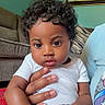 baby, child, curly_hair, indoor, onesie, couch, carpet, hand, person, portrait, expression, room, wall_art, colorful, holding, infant, cute, sitting, adult, living_room