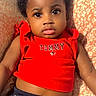 Janylah is registered to the contest to win money with this photo: toddler, child, baby, girl, red_top, navy_shorts, hair_clips, curly_hair, cushion, patterned_fabric, indoor, portrait, cute, expressive_eyes, casual_clothing, relaxed, seated, person, closeup, fashion