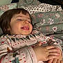 toddler, child, smile, happy, hands, bed, blanket, pajamas, christmas_pattern, indoor, cozy, face, person, young_child, sleepwear, cute, expression, holiday, resting, comfort