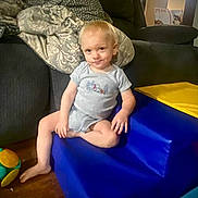 Bentley Kingston is registered to the contest to win money with this photo: toddler, child, indoor, blue_chair, yellow_chair, toy, blanket, couch, floor, smiling, casual, playroom, furniture, person, footwearless, shorts, onesie, blond_hair, cute, relaxed
