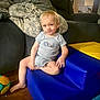 toddler, child, indoor, blue_chair, yellow_chair, toy, blanket, couch, floor, smiling, casual, playroom, furniture, person, footwearless, shorts, onesie, blond_hair, cute, relaxed