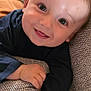 baby, child, smiling, face, couch, hand, long_sleeve_shirt, happy, indoor, close_up, skin, person, infant, portrait, young_child, texture, fabric, relaxing, cute, comfortable