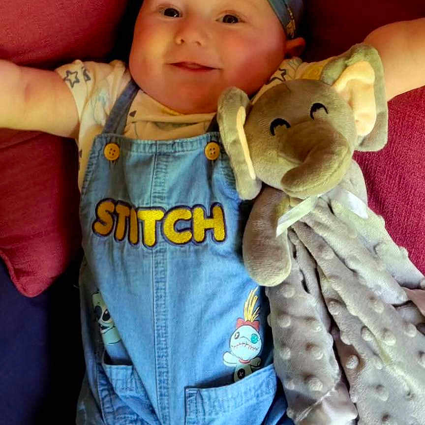 Anorah joined the competition — help win amazing prizes! baby, blue_background, child, clothing, cushion, cute, denim, elephant, face, happy, headband, indoors, infant, lying_down, overalls, plush_toy, portrait, red_cushion, smiling, soft_toy