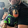 man, dog, glasses, sweater, dinosaur_print, ball, indoor, smiling, embrace, pet, couch, furniture, happy, casual, beard, short_hair, black_shirt, paw, toy, close_up