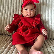 Shaeleigh is registered to the contest to win money with this photo: baby, infant, red_dress, headband, bow, couch, furniture, barefoot, knitted_clothing, child, cute, portrait, indoor, seated, young_child, expression, skin, face, legs, hands