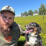 Gauge is registered to the contest to win money with this photo: man, beard, cap, dog, outdoor, field, flowers, grass, sunny, blue_sky, smile, tongue_out, pet, nature, casual_clothing, happy, animal, portrait, greenery, daylight
