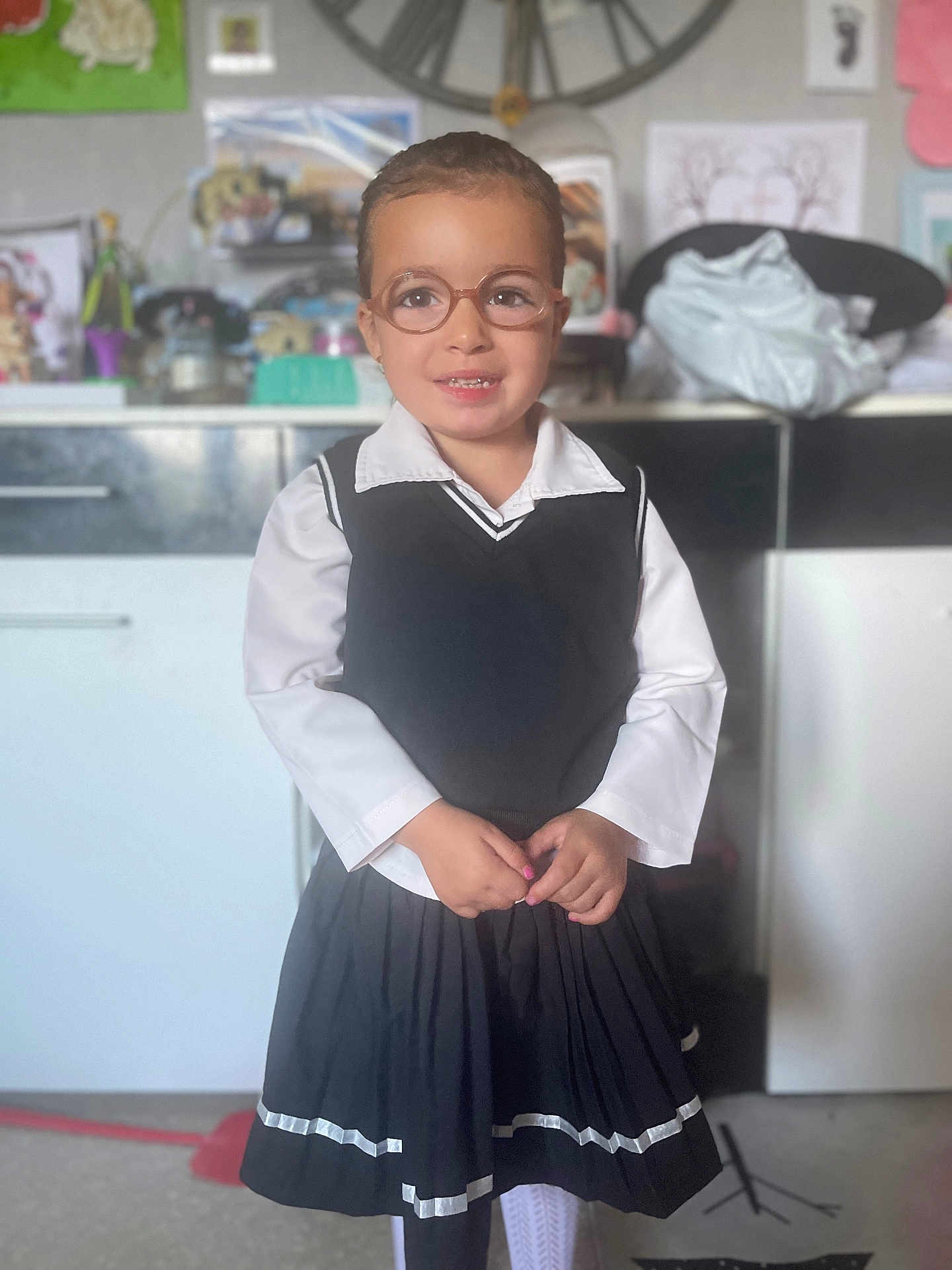 Serena a rejoint le concours — aidez-le/la à gagner de superbes lots ! child, glasses, smile, school_uniform, pleated_skirt, white_shirt, black_vest, indoor, home, floor, cabinet, clock, drawing, toy, person, portrait, standing, cute, happy, tights