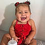 baby, child, smiling, red_clothing, romper, bottle, milk, sitting, indoors, happy, gold_sandals, hair_bows, infant, cute, playful, portrait, skin, person, young_child, bed
