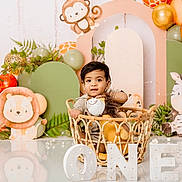 Damian is registered to the contest to win money with this photo: baby, basket, balloon, birthday, celebration, child, cute, decorations, face, first_birthday, floor, gift, indoor, jungle_theme, lion, plush_toy, smile, toddler, toy, wicker