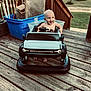 baby, baby_boy, blue_container, child, daylight, footwearless, fun, grass, happy, outdoor, person, plastic, playtime, seat, smiling, stairs, steering_wheel, toy_car, wood, wooden_deck