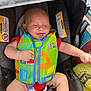 baby, car_seat, child, clothing, colorful, cute, happy, indoors, infant, padding, person, plastic_bag, red_shirt, safety, seatbelt, sitting, small_child, smiling, swim_vest, toy