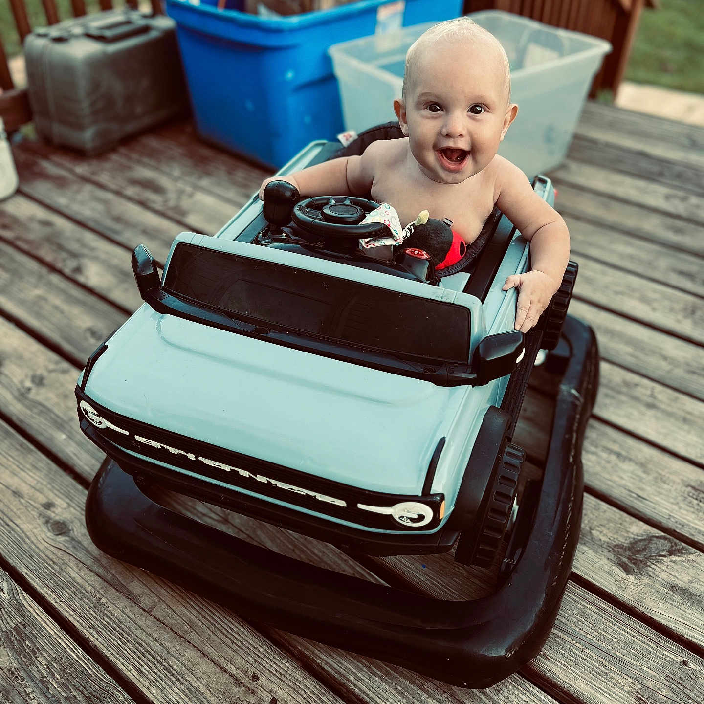 Raedynn is registered to the contest to win money with this photo: baby, child, container, cute, deck, fence, fun, happy, infant, outdoor, person, plastic, play, seat, smiling, steering_wheel, storage, toy_car, vehicle, wooden