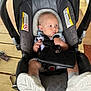 baby, baby_accessory, baby_boy, baby_clothing, car_seat, child, cute, footwear, indoors, infant, infant_carrier, person, portrait, safety_harness, seat_belt, sitting, socks, soft_padding, wooden_table, young_child