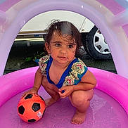 Emy participe au concours pour gagner de l'argent avec cette photo : toddler, child, inflatable_pool, pink, soccer_ball, wet_hair, squatting, outdoor, play, water, barefoot, summer, toy, colorful_clothing, expression, vehicle_tire, curious, small_ball, fun, daylight