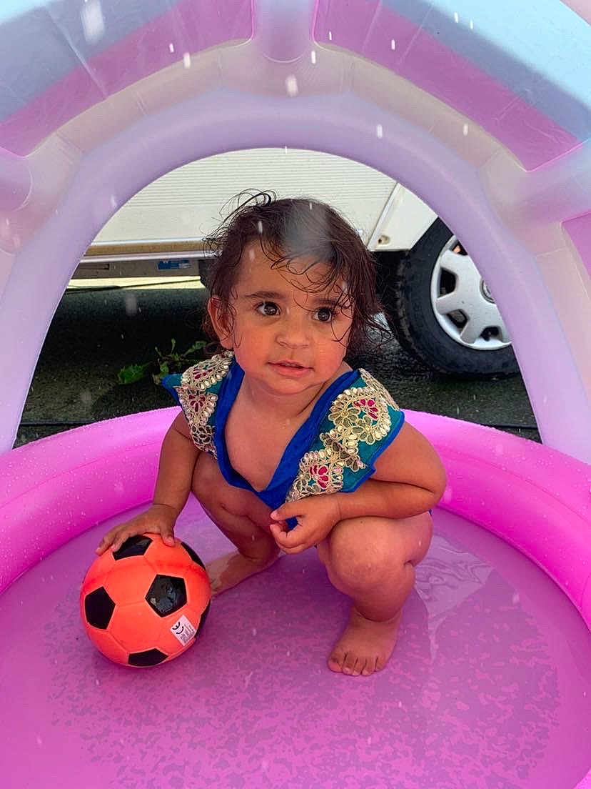 Emy participe au concours pour gagner de l'argent avec cette photo : toddler, child, inflatable_pool, pink, soccer_ball, wet_hair, squatting, outdoor, play, water, barefoot, summer, toy, colorful_clothing, expression, vehicle_tire, curious, small_ball, fun, daylight