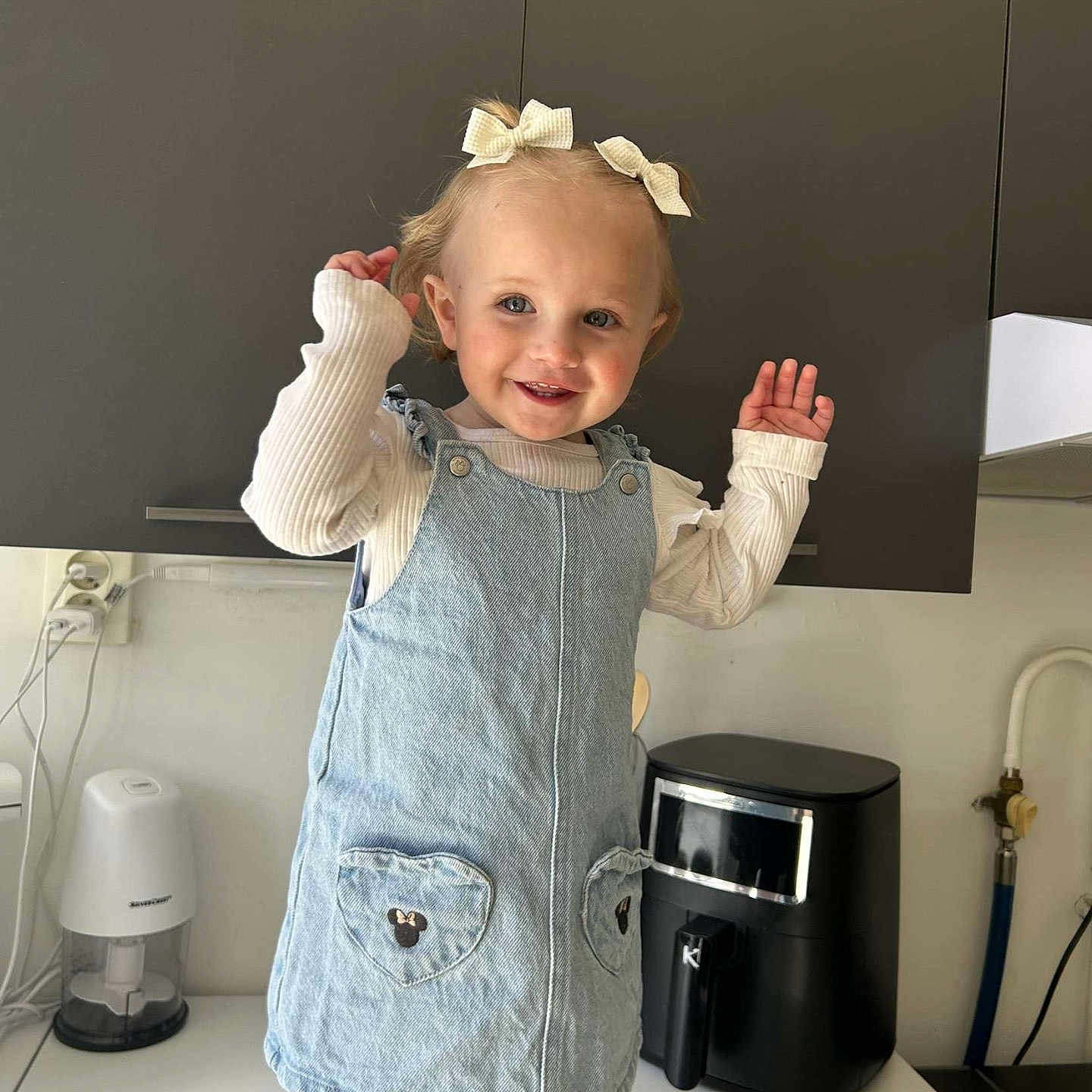 Analia participe au concours pour gagner de l'argent avec cette photo : appliance, bows, cabinet, child, clothing, countertop, cute, denim_dress, face, girl, hair, happy, indoor, kitchen, person, portrait, smiling, standing, toddler, white_socks